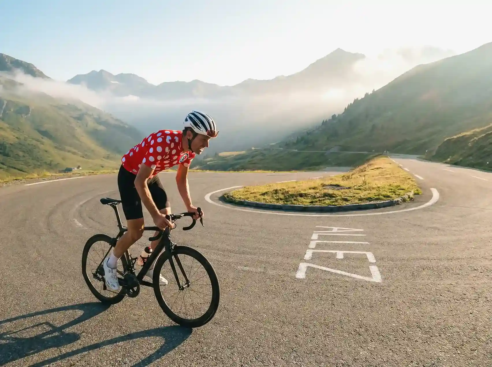 Cycliste grimpant un col de montagne en lacets dans un paysage alpin spectaculaire